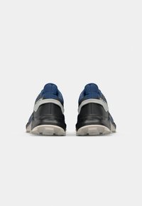 Baskets de sport bleues et noires avec une tige texturée, un talon rembourré et une semelle robuste. Détail du logo argenté sur les côtés.