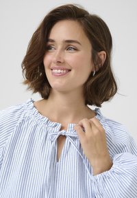 Blouse rayée bleu et blanc avec encolure élastique et détail en forme de trou de clé, dotée de manches bouffantes et d'une texture de tissu douce.