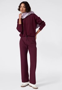 Conjunto deportivo burdeos que incluye una sudadera de corte holgado y pantalones ajustados. Combinado con una bufanda lila clara y zapatillas blancas.