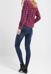 Röd och marinblå rutigt flanellskjorta kombinerad med mörka skinny jeans och svarta ankelboots. Har långa ärmar och en figursydd design.