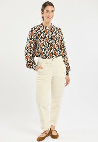 Black and orange patterned long-sleeve blouse paired with cream corduroy pants and brown shoes, showcasing relaxed fit and button detailing.