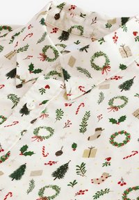 Chemise à boutons avec motif festif comprenant des couronnes, du houx, des cannes en bonbon, des boîtes cadeaux, des bas et des branches de pin sur fond crème.