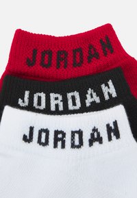 Kolm paari lühikesi sokke punases, mustas ja valges värvitoonis. Igal sokipaari on kudumisse sisse kootud tekst "JORDAN" kontrastse musta või valge tähega.