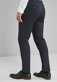 Tengerészkék nadrág, szabott fazonban, sima anyagból készült. Hátul gombos zsebbel és kontrasztvarrással díszítve. Fekete bőr cipővel párosítva.