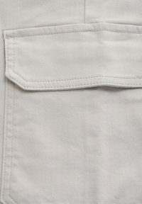 Ljusgrått tyg med en texturerad yta, med en ficka i lappstil med en platt topp och kontrasterande sömnadsdetaljer.