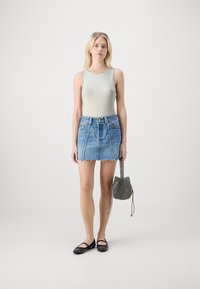 Lys grønne ermeløse bodysuit, blå denim miniskjørt med frayed kant, sorte flate sko med nagledetaljer, og en liten mønstret veske.
