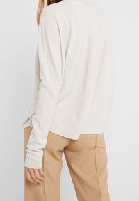 Pull en maille beige clair avec une coupe décontractée, doté de manches longues et d'un col rond. Texture douce, design à ourlet fendu et détails de couture minimalistes.