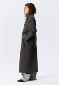 Lang grå ullkåpe med bred krage, to knapper og sidelommer. Glatt tekstur med en midtlang silhuett.