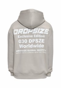 Sudadera con capucha beige con texto blanco en la espalda que dice "DROPSIZE Edición Exclusiva 030 DPSZE Mundial" y enumera las principales ciudades.