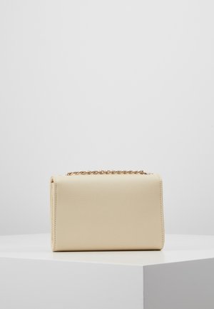 Rektangulær beige læderhåndtaske med en tekstureret overflade og et gyldent kædehåndtag, placeret på en hvid piedestal mod en ensfarvet baggrund.