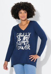 Marineblauw T-shirt met lange mouwen en V-hals, met daarop in zilveren letters "CRAZY IS MY SUPER POWER." De stof lijkt zacht en glad te zijn.