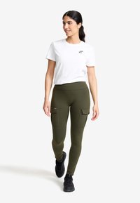 Olivgröna cargoleggings med sidofickor, parat med en vit kortärmad t-shirt med en liten logotyp på bröstet. Svarta sneakers.