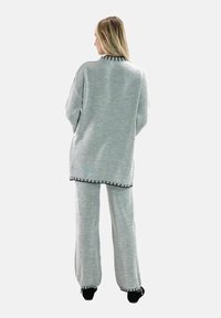 Conjunto de loungewear de punto gris claro que incluye una camiseta de manga larga y pantalones a juego, con ribetes negros en el dobladillo y los puños.