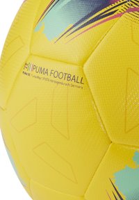 Pallone da calcio giallo senza PVC con superficie testurizzata; presenta accenti blu e viola e informazioni sul marchio stampate in nero.