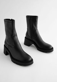 Botas negras de cuero hasta el tobillo con cremalleras laterales, tacones gruesos, puntera redondeada y suela de goma texturizada, con detalles de costura en contraste.