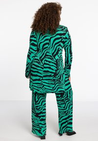 Groen en zwart gestreepte outfit bestaande uit een lange top met een rechte snit en een losse broek, gemaakt van een gestructureerde stof.