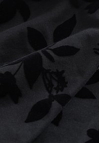 Fekete szövet bársonyos virágmintával, levelekkel és virágokkal. A textúra puha, sima felületű és enyhén fényes.