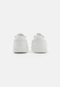 Zapatillas de cuero blanco con una textura suave, forma redondeada y suelas de goma planas. El diseño incluye sutiles detalles de costura.