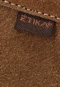 Tejido de ante marrón con una superficie texturizada y una pequeña etiqueta tejida que muestra "ETIKA" en marrón, cosida en el borde.