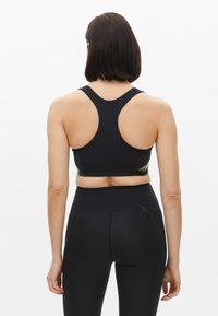 Sujeción deportiva negra con un diseño de espalda nadadora, hecha de una tela suave. Presenta una silueta ajustada y un sutil detalle de costuras.