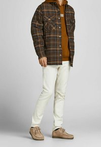 Brun rutigt flanellskjorta över en brun hoodie, ihop med vita jeans och tan mockaskor. Inkluderar fickor och knapplösningar.