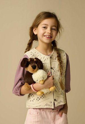 Young girl with braided hair, wearing a striped shirt and knitted vest, holding plush dog and duck toys against beige background.