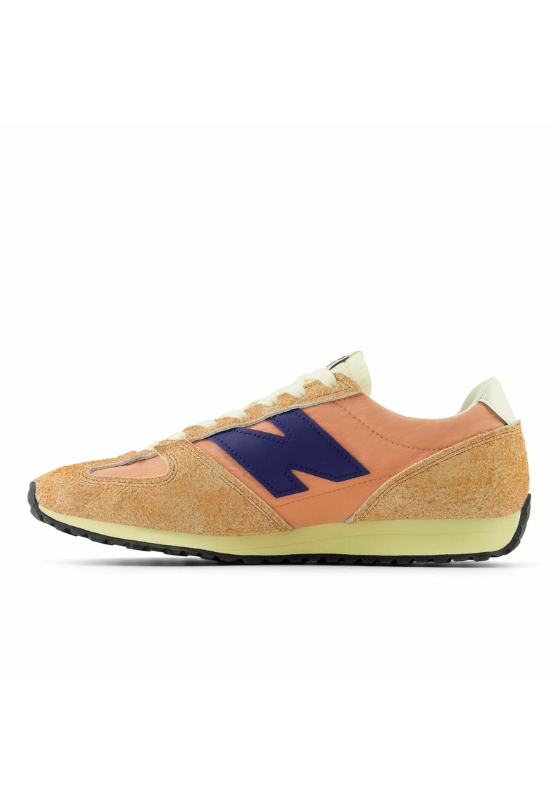 Orange och beige sneaker med en mockaliknande textur, lila logotyp och krämfärgade detaljer. Har en svart gummisula och snörning.