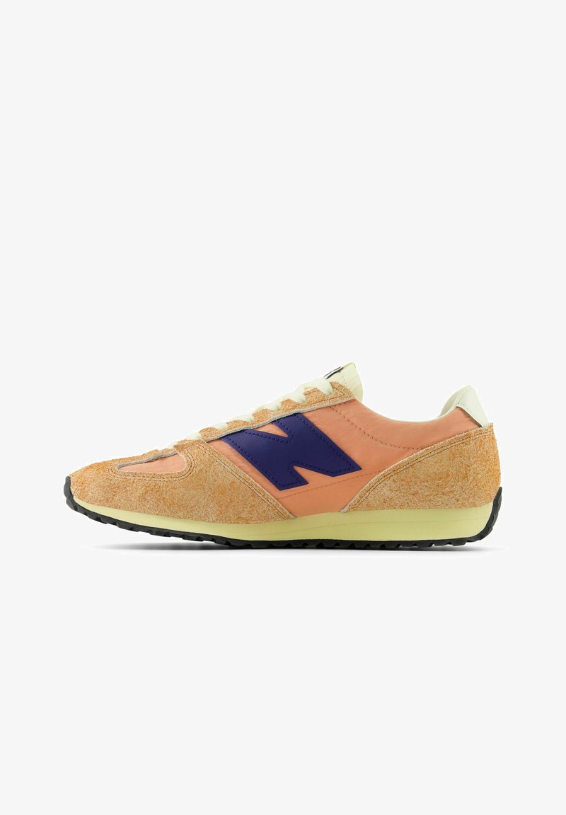 Orange och beige sneaker med en mockaliknande textur, lila logotyp och krämfärgade detaljer. Har en svart gummisula och snörning.