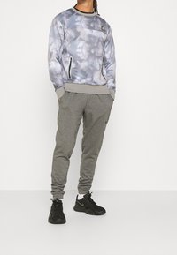 Sudadera gris con efecto tie-dye, con puños y cuello acanalados; combinada con pantalones de chándal grises con cordón y bolsillos laterales; zapatillas negras.