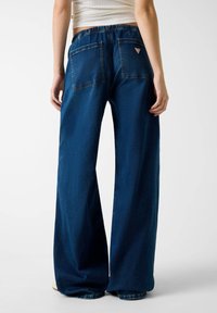 Tumedat sinised laiad denimpüksid mugava lõikega, millel on kaks tagumist taskut ja paremas taskus õmmeldud silt. Elastne vöökoht.