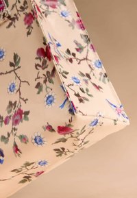 Torba tote w kwiaty z beżowego materiału z czerwonymi i niebieskimi wzorami kwiatowymi. Strukturalny kształt z widocznym szyćmi i akcentami.