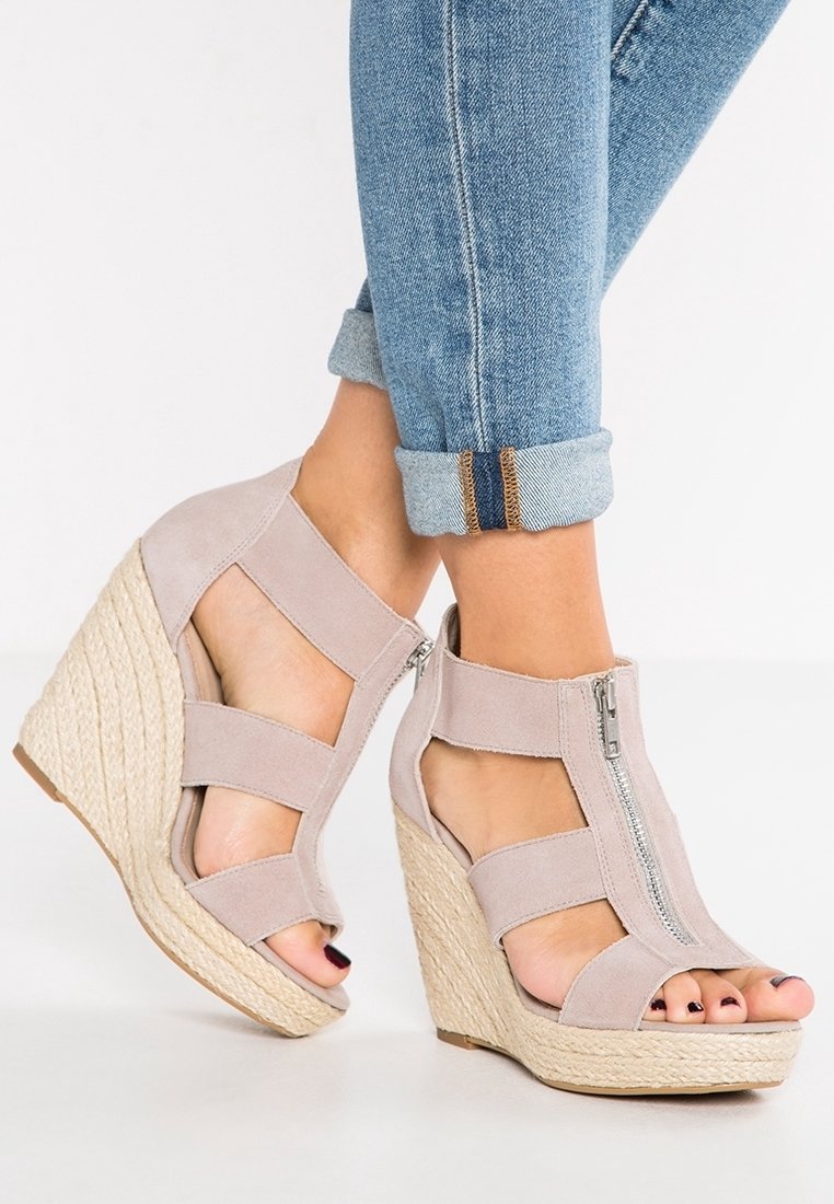 Sandale à talon compensé beige en daim avec fermeture éclair, côtés ajourés et base en corde texturée. Présente un design à bout ouvert.
