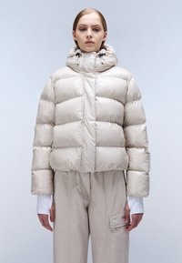 Giacca puffer accorciata beige con collo alto e cappuccio. Presenta una finitura liscia e lucida e sezioni trapuntate per l'isolamento.