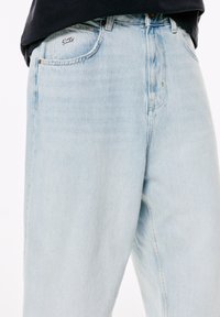 Lyseblå denim jeans båret med en sort skjorte, der viser forlommer og bæltestropper på en ensfarvet hvid baggrund.