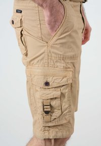 Shorts cargo beiges en tissu léger dotés de plusieurs poches, d'une surface texturée et d'une sangle réglable avec boucle sur le côté.