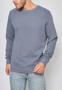 Sweatshirt gris à manches longues en tissu texturé, avec un col et des poignets ribbés, présentant une coupe décontractée et un design simple.
