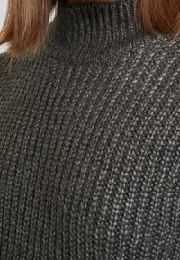 Pullover di maglia grigio scuro con colletto alto, caratterizzato da un motivo a coste testurizzato e tessuto morbido e spesso. Inquadratura ravvicinata del materiale.