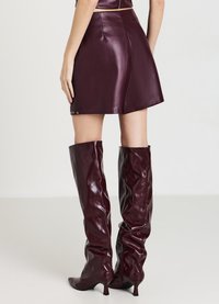 Gonna mini in pelle bordeaux con una texture liscia e dettagli a scatto laterale, abbinata a stivali lucidi bordeaux al ginocchio con punta affilata.