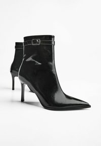 Pereche de bocanci negri lucioși cu vârf ascuțit, toc înalt subțire și curea cu cataramă în jurul gleznei superioare.