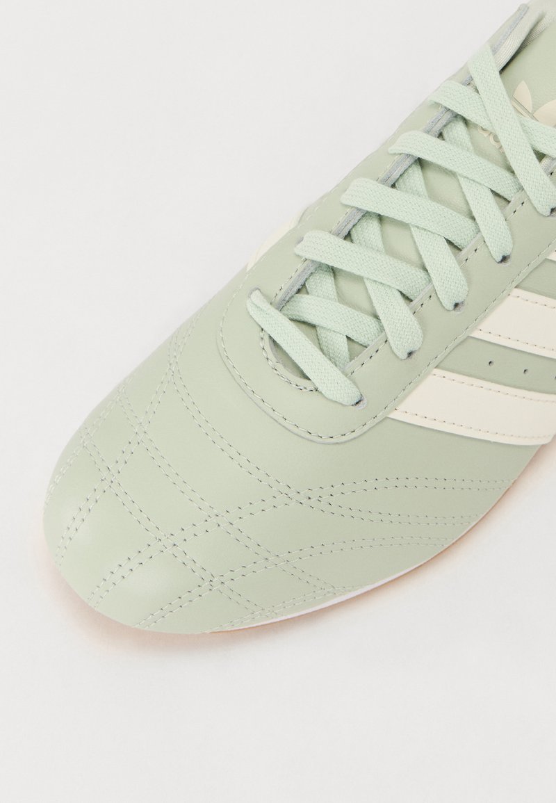 Botín de fútbol color verde menta con cuero texturizado, franjas blancas y cordones a juego. Presenta costuras acolchadas y una suela de goma.