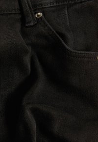 Svart denimtyg med en ficka, slät textur, subtil vävstruktur och en metallknapp nära midjan.