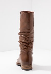 Botte haute jusqu'au genou en cuir marron avec un design décontracté, fermeture éclair latérale et talon empilé. Texture lisse avec un détail de couture subtil.