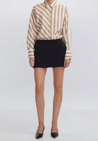 Camicia a righe a maniche lunghe in beige e bianco, abbinata a una mini gonna nera aderente. Tacchi neri a punta completano l'outfit.