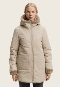 Beige Daunenjacke mit Reißverschluss, zwei großen Taschen und einer Kapuze, die mit Kunstfell gefüttert ist. Eigenschaften sind strukturierte Ärmel und eine gerade Passform.
