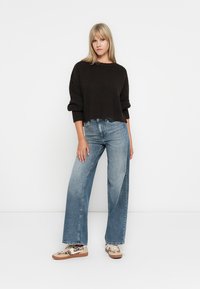Svart strikket cropped genser, lyseblå vide jeans og mønstrede sneakers. Glatt tekstur og avslappet passform med fremtredende mansjetter.