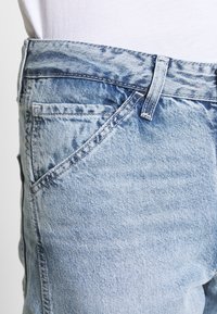 Närbild av en urblekt blå denimjeansficka och bältesloopen, som bärs med en vit topp.