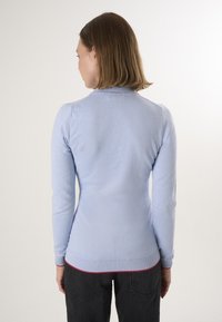 Maglione a maglia azzurro chiaro con un collo alto, design aderente, maniche lunghe e orlo a coste accentuato di rosso nella parte inferiore.