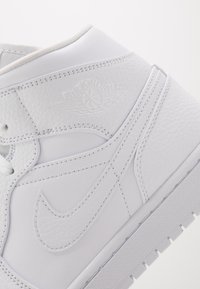Gros plan d'une sneaker Air Jordan en cuir blanc montrant le logo Wings embossé et le swoosh Nike cousu sur le côté avec une semelle texturée.