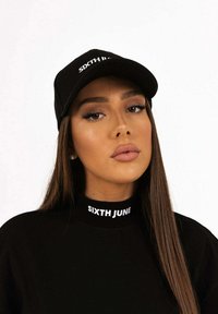 Cappello nero con il logo "SIXTH JUNE" sulla parte anteriore, indossato con un pullover nero coordinato che presenta lo stesso logo sul colletto. Texture liscia.