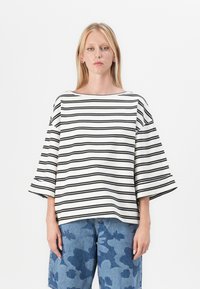 Stripet overdimensjonert topp i krem og svart, med vide ermer og båthals; kombinert med blå mønstrete denimshorts.